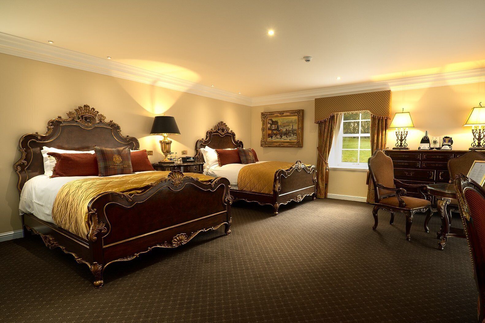 A hotel room with two ornate beds, a desk, and a chair.