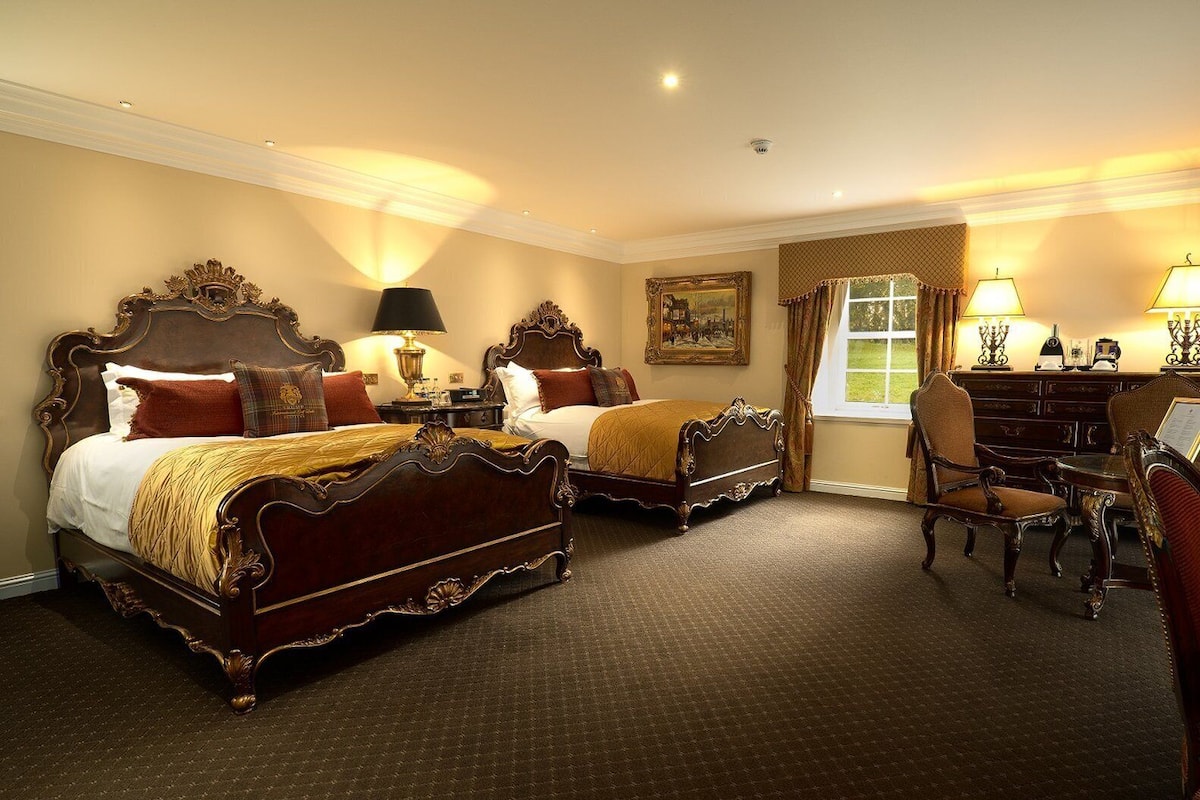 A hotel room with two ornate beds, a desk, and a chair.