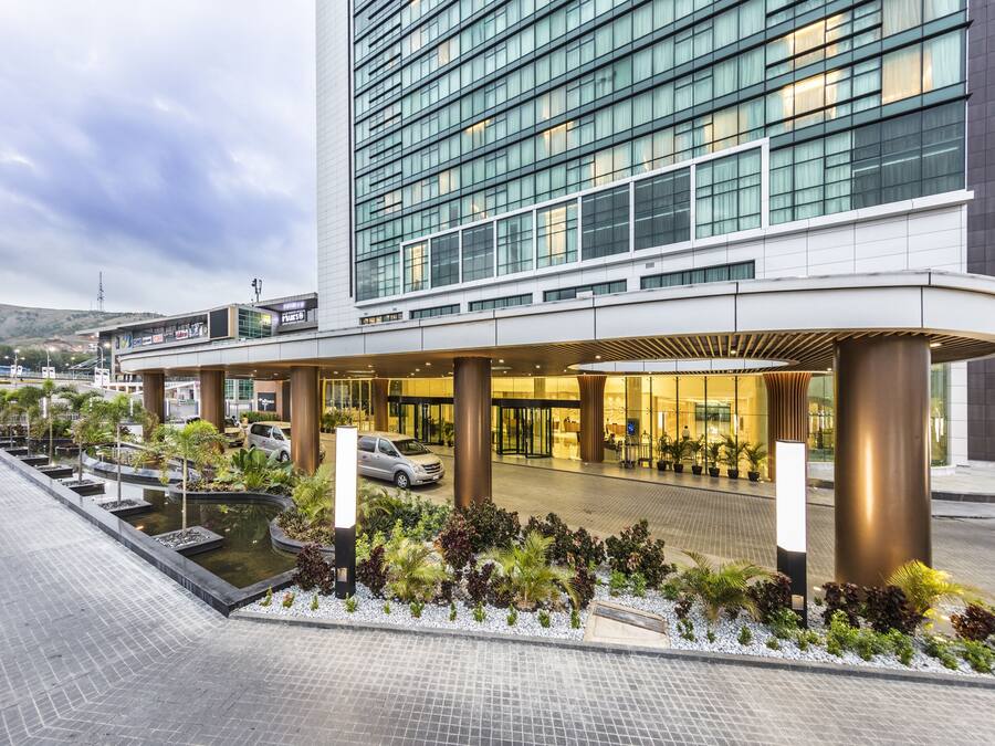 A modern hotel with a glass facade, a landscaped entrance, and a parking area.