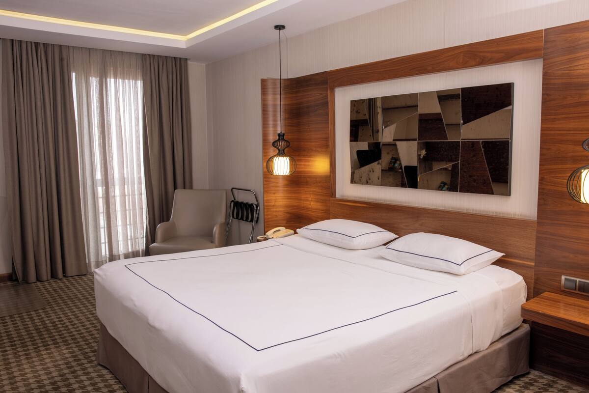 Habitación de hotel con una cama grande, cabecera de madera, un espejo y un escritorio con lámpara.