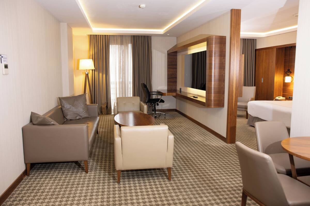 Una habitación de hotel con sofá, sillones, una mesa de comedor, un espejo y una cama.