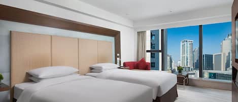Ein Hotelzimmer mit zwei Betten, einem großen Fenster mit Blick auf die Stadt, einem roten Sessel und einem kleinen Tisch mit einer Vase.