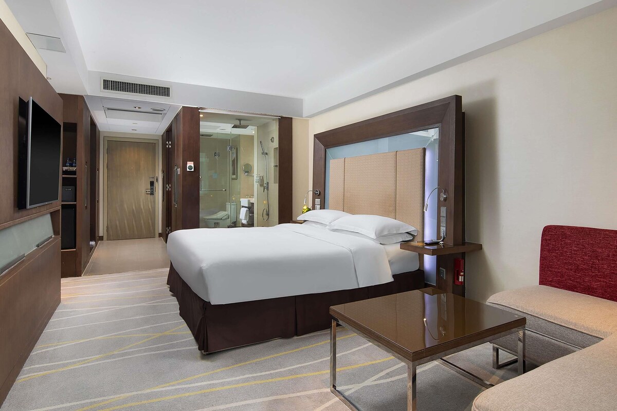 A hotel room with a bed, a bedside table, a mirror, a TV, and a shower area.