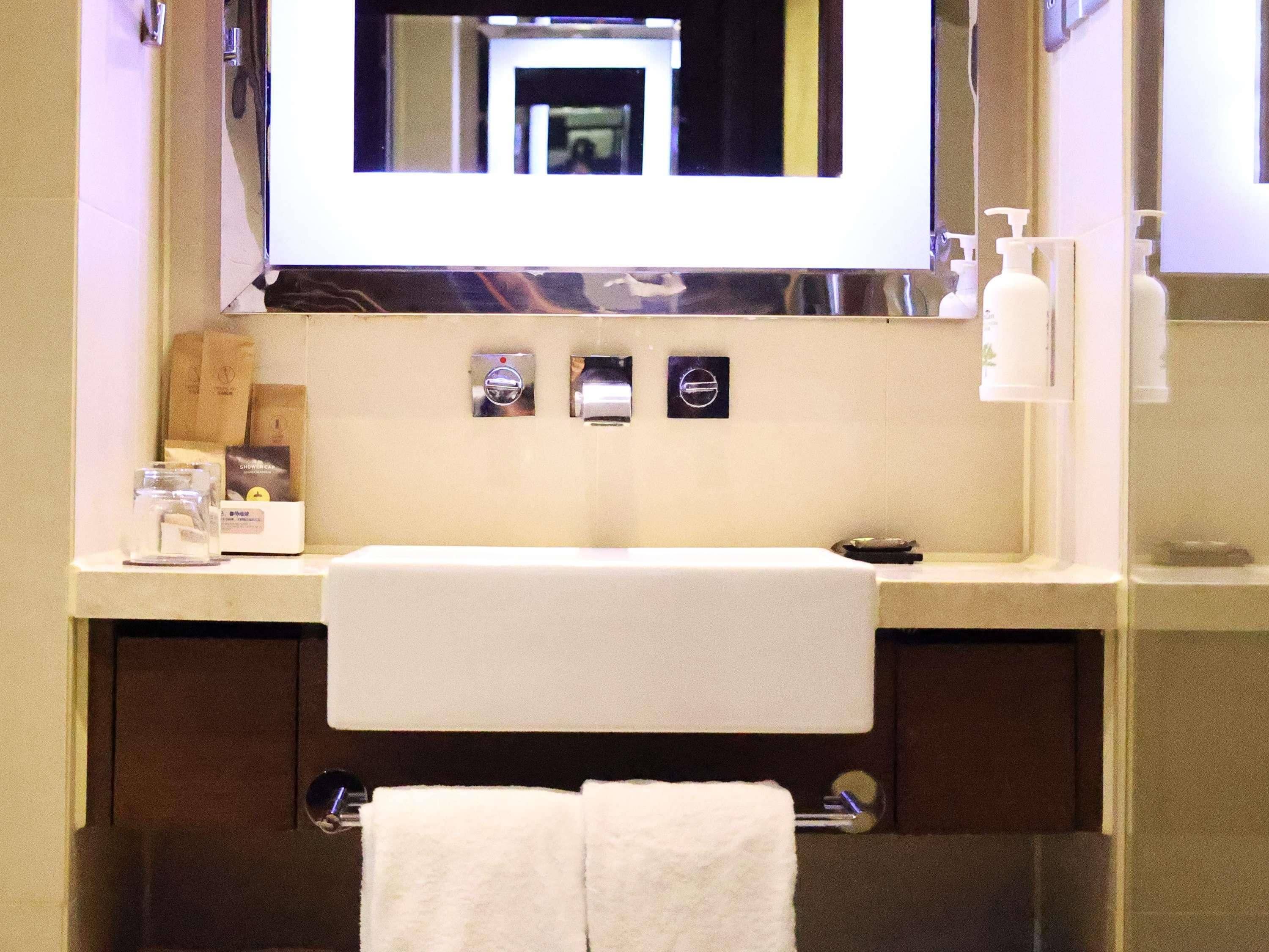 A bathroom with a large mirror, a sink, and a towel rack.