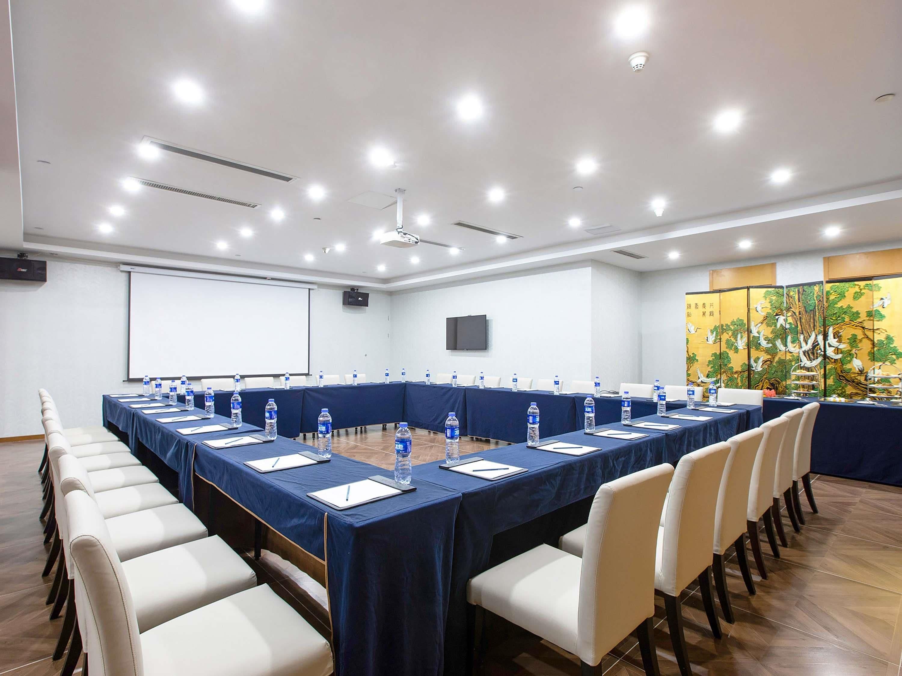 A conference room with a long table, chairs, water bottles, and a projector screen.