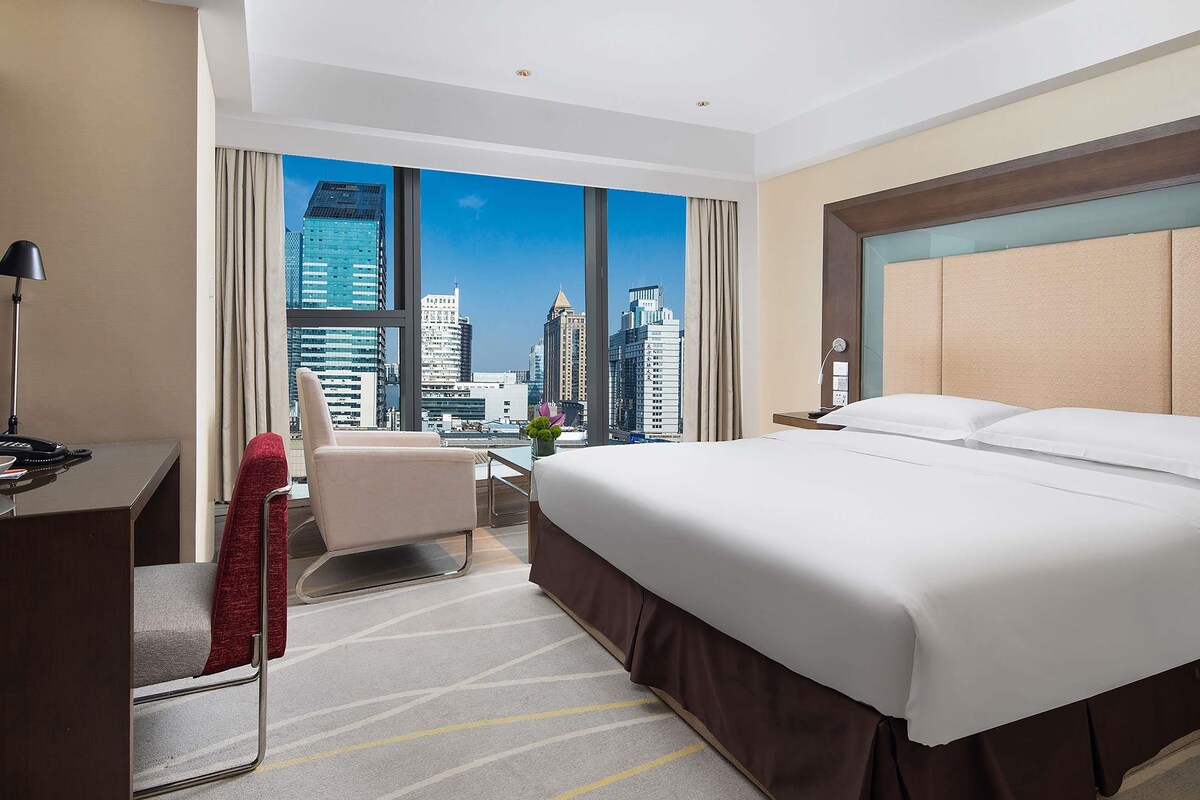Une chambre d’hôtel avec un grand lit, un bureau, une chaise et une vue sur le panorama urbain.