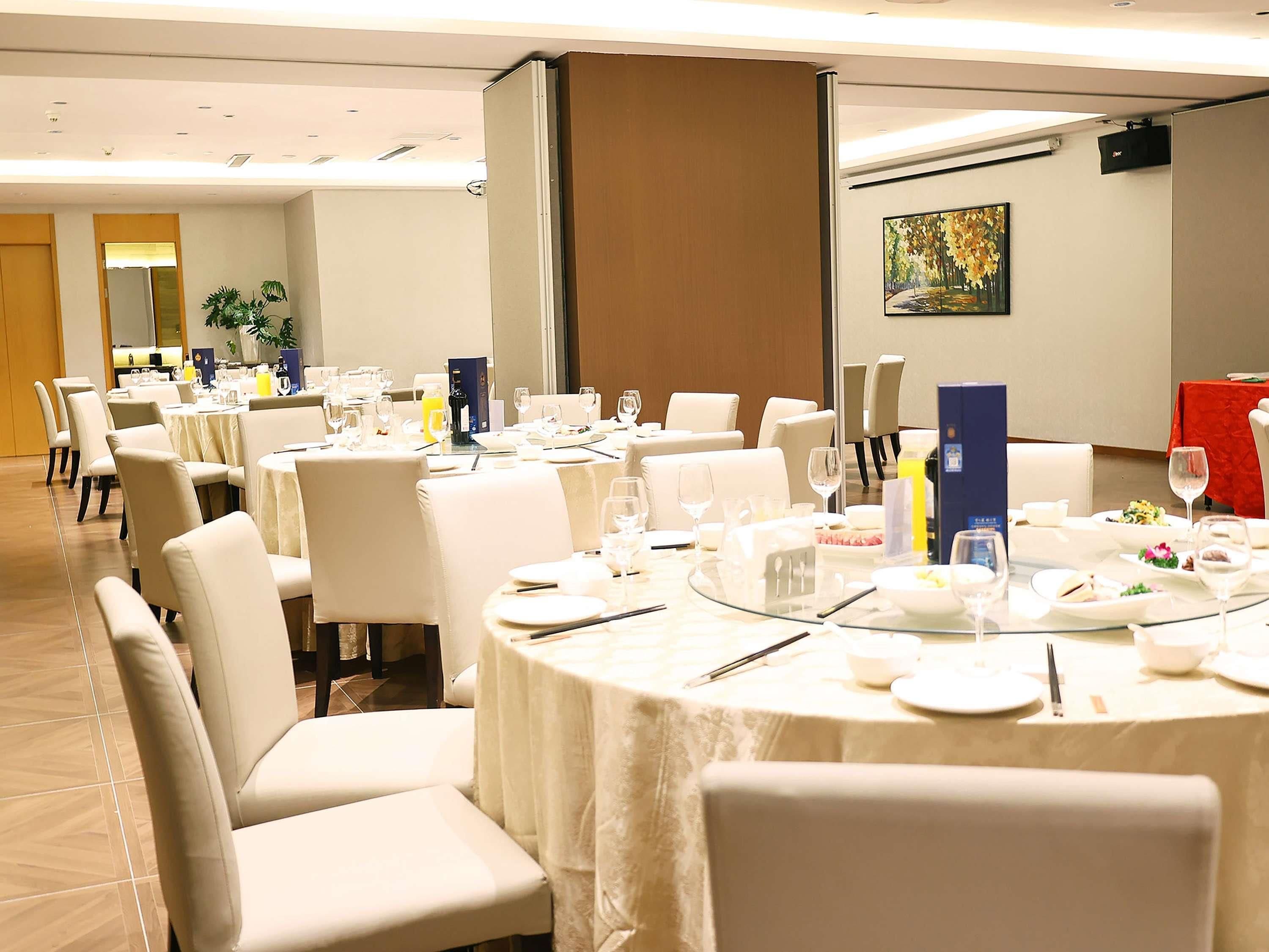 A banquet hall with round tables set for dining, white chairs, and a large painting on the wall.