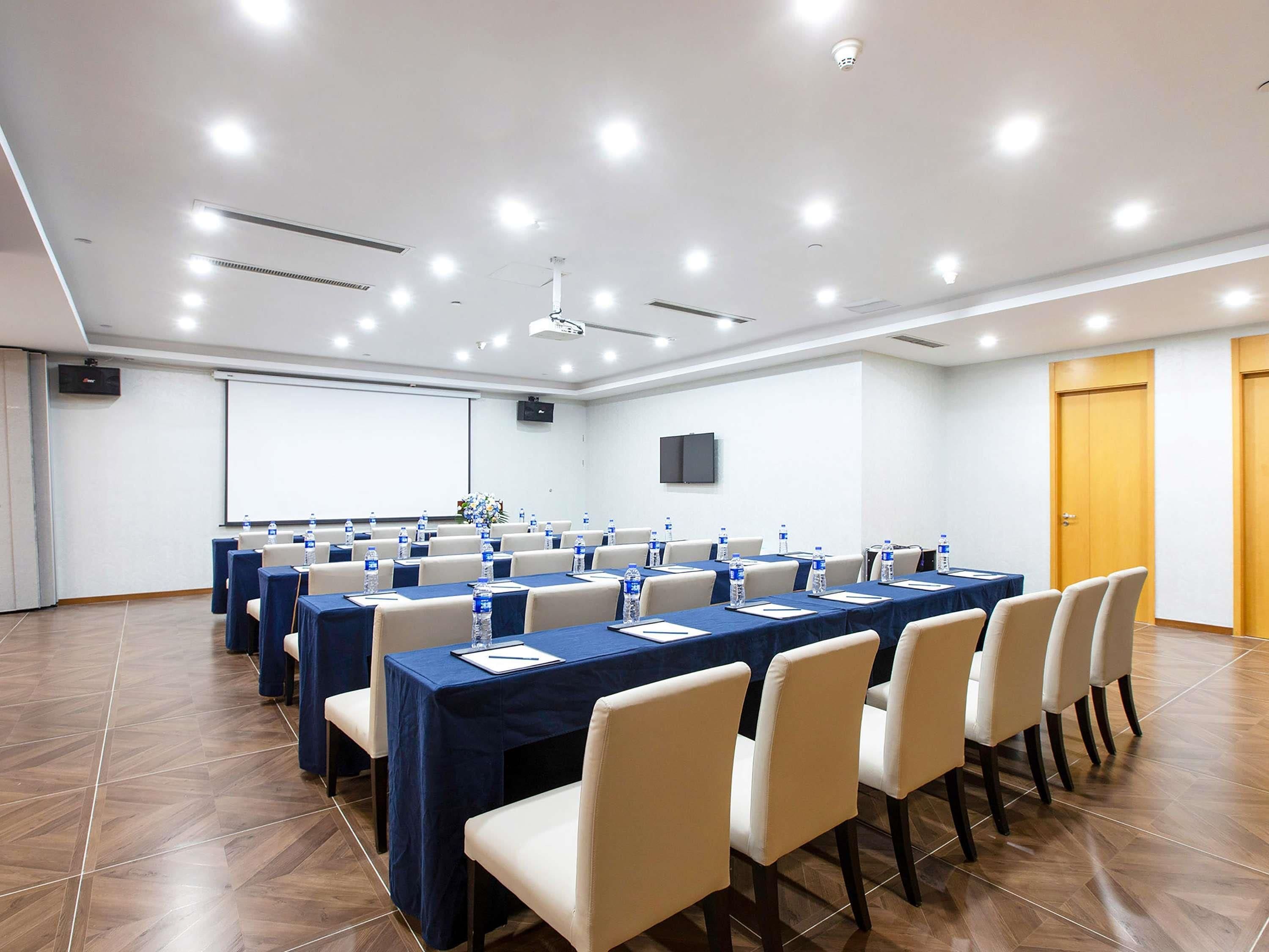 A conference room with multiple tables, chairs, a projector screen, and a whiteboard.