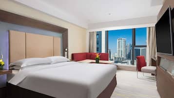 A hotel room with a large bed, a red sofa, a TV, and a city view.