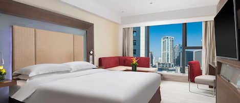 A hotel room with a large bed, a red sofa, a TV, and a city view.