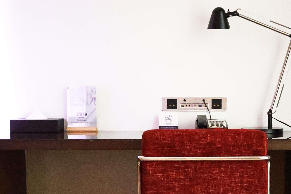 A hotel reception desk with a red upholstered chair, a black desk lamp, and a white sign with text.