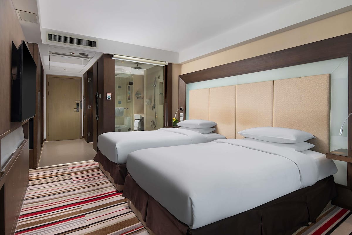 A hotel room with two beds, a TV, a shower, and a striped carpet.