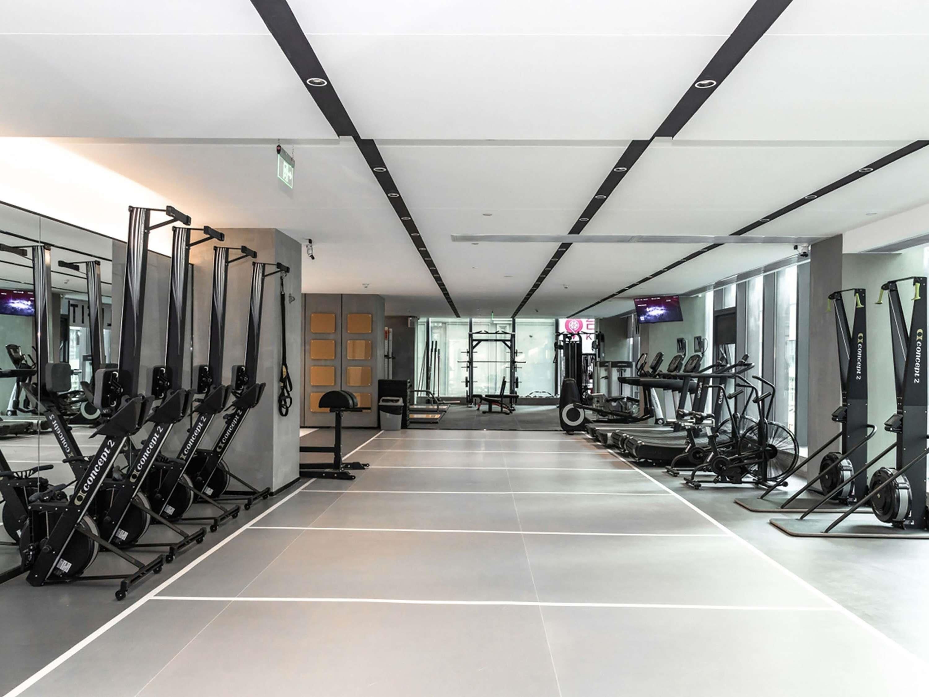 Une salle de sport moderne équipée de machines de cardio, d’appareils de musculation et de miroirs aux murs.