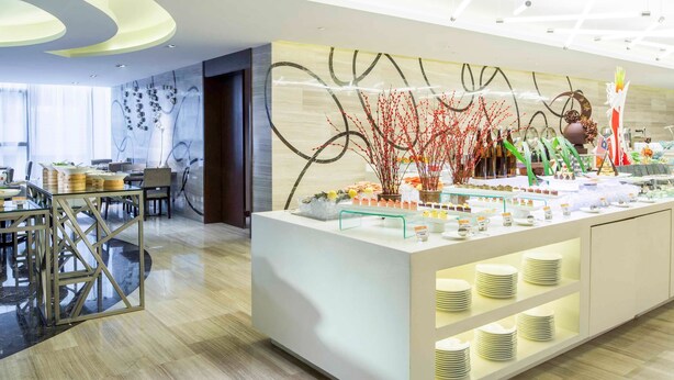 A modern hotel lobby with a reception desk, seating area, and a buffet with various food items. - Novotel Nanjing Central Suning (Nanjing)