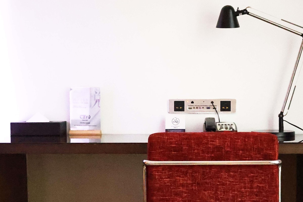A hotel reception desk with a red upholstered chair, a black desk lamp, and a white sign with text.
