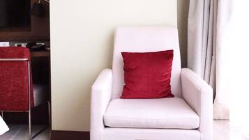 Un sillón blanco con un cojín rojo en una habitación con un televisor de pantalla plana montado en la pared y una silla roja al fondo.