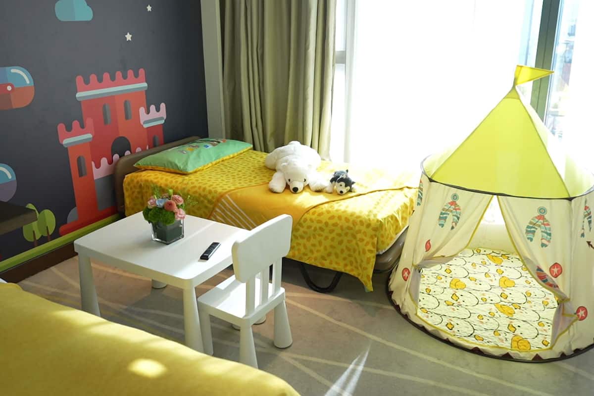A child's bedroom with a bed, a small table, a chair, a tent, and a wall with a castle mural.