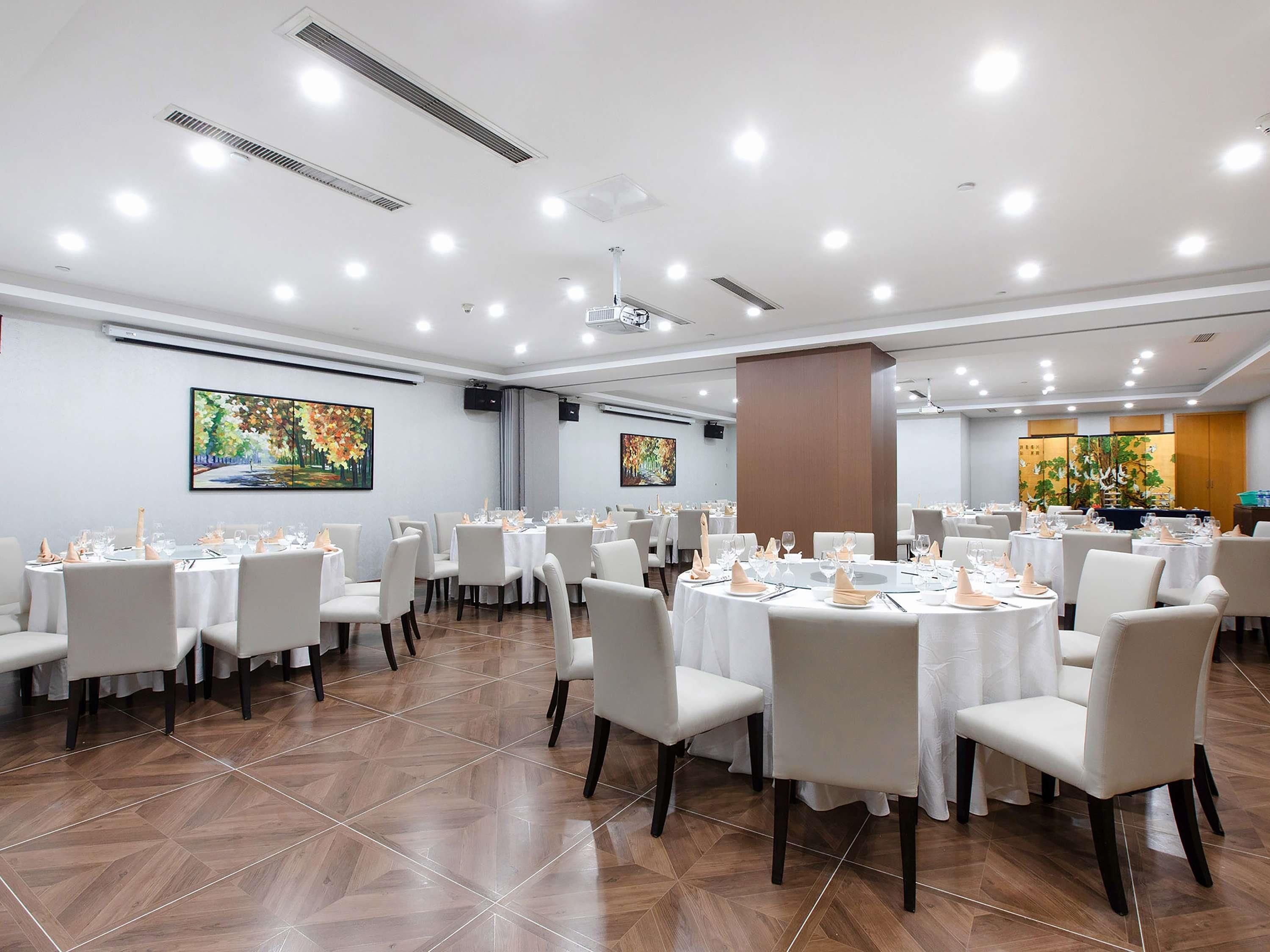 Una spaziosa sala da banchetti con diversi tavoli rotondi apparecchiati per la cena, sedie bianche e un pavimento lucido a spina di pesce.
