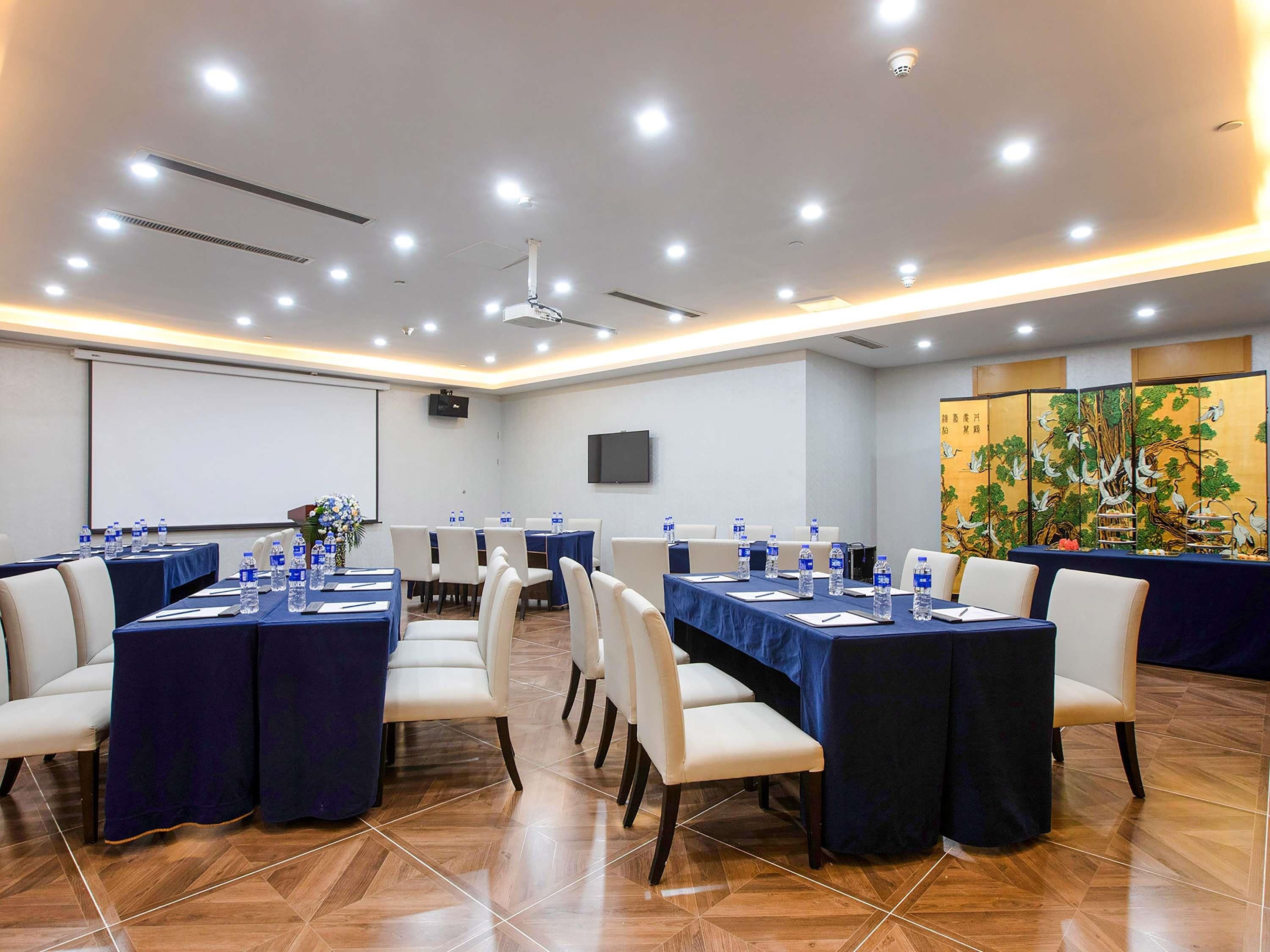 Un salón de conferencias con mesas, sillas, botellas de agua, una pantalla de proyector y una pantalla decorativa con pájaros.