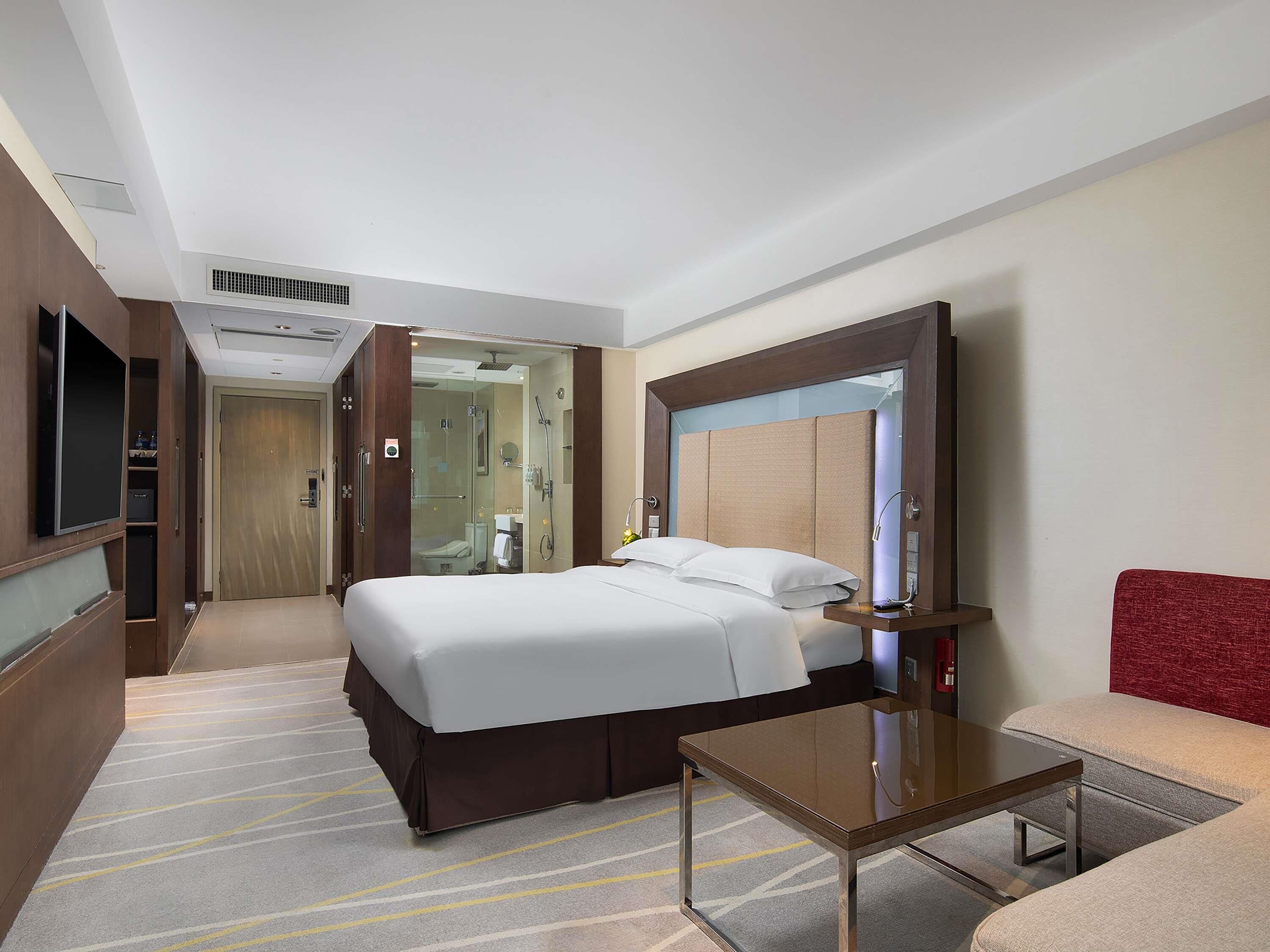 Une chambre d’hôtel comprenant un lit, une table de chevet, un miroir, une télévision et un espace douche.