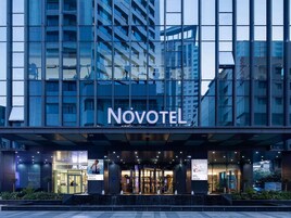 Un hotel moderno con un llamativo letrero de 'Novotel', amplias ventanas de vidrio y una entrada bien iluminada.