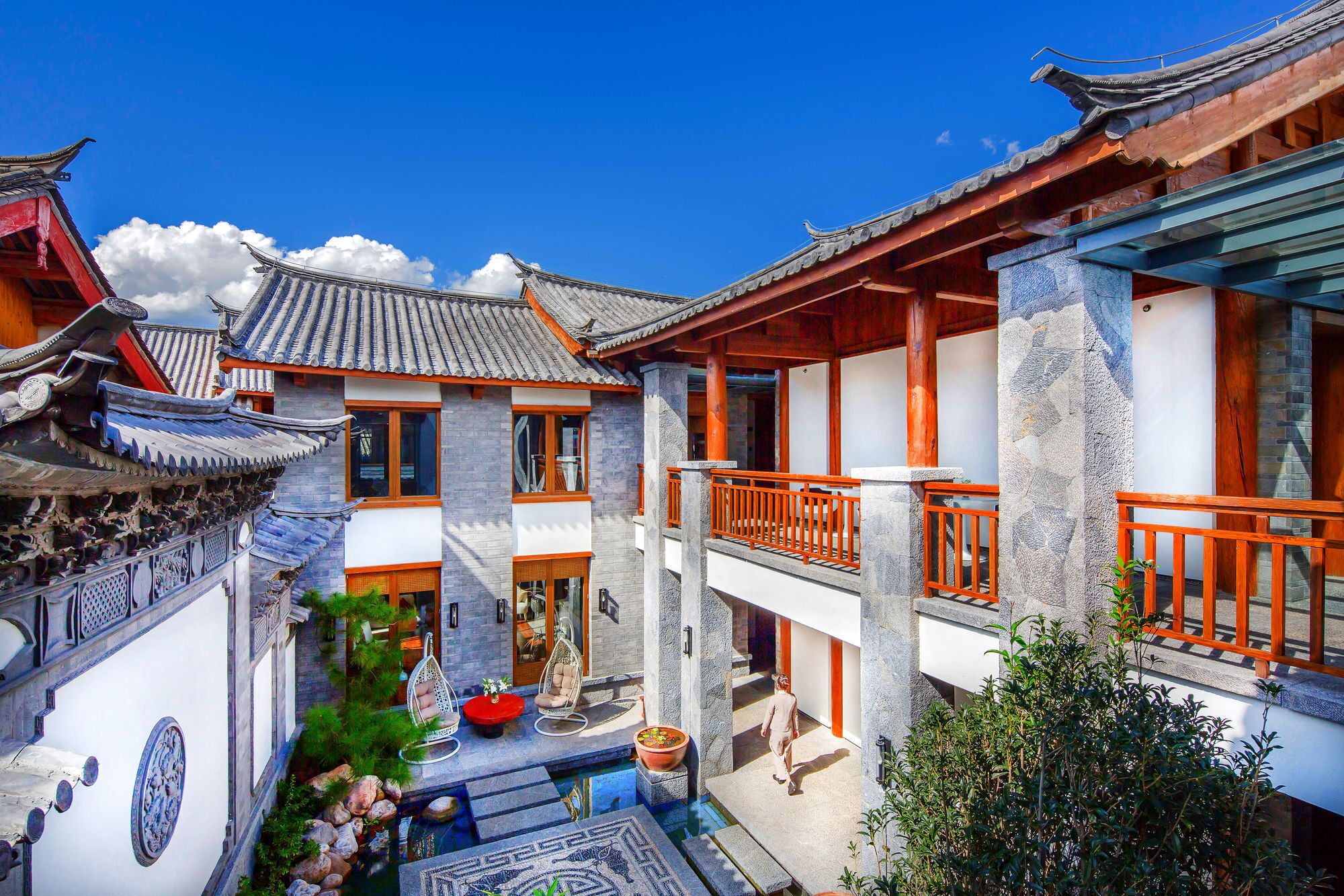 A traditional courtyard with a stone fountain, hanging chairs, and a wooden balcony.