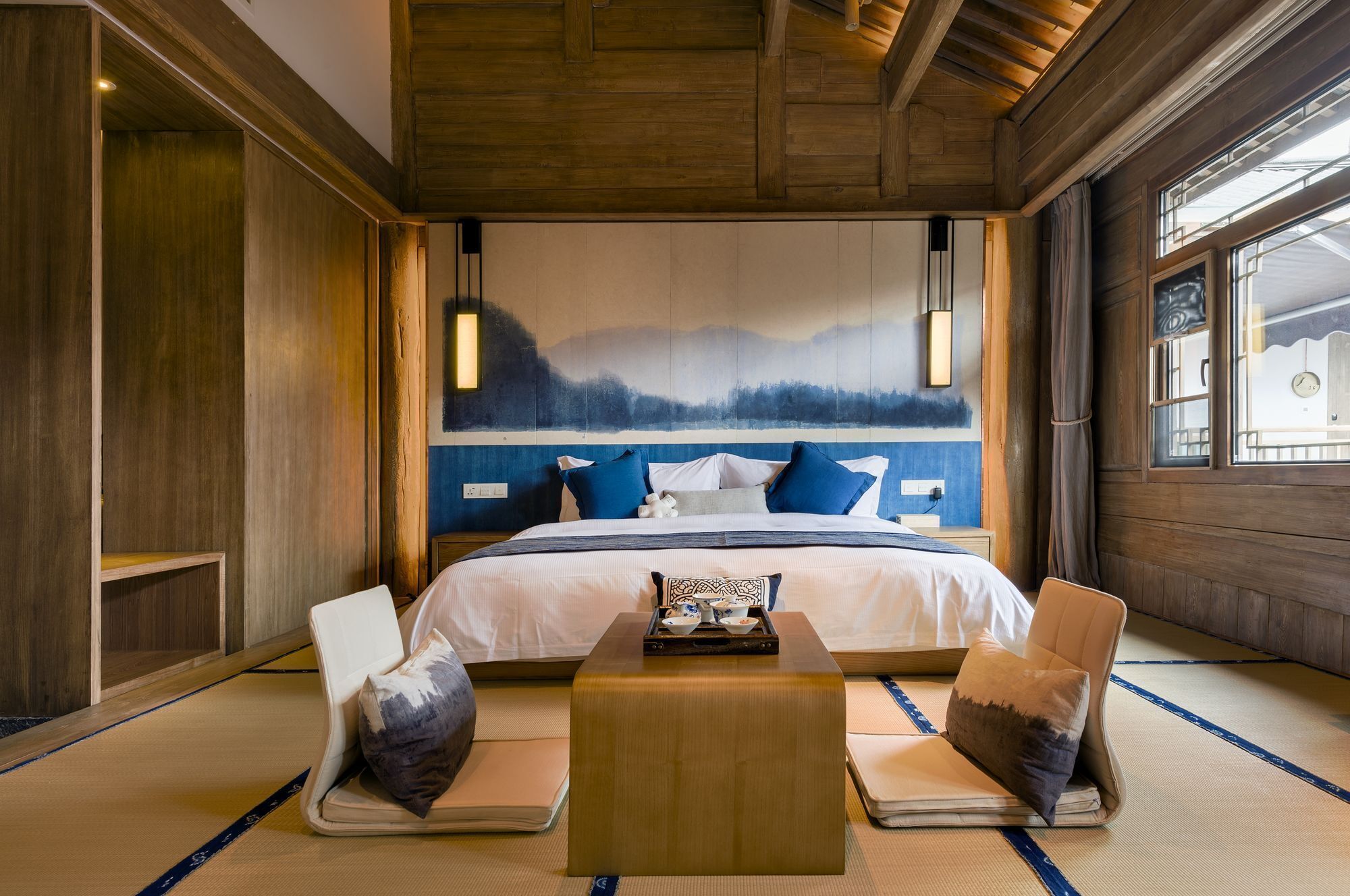 A bedroom with a bed, two chairs, a small table, and a large painting on the wall.