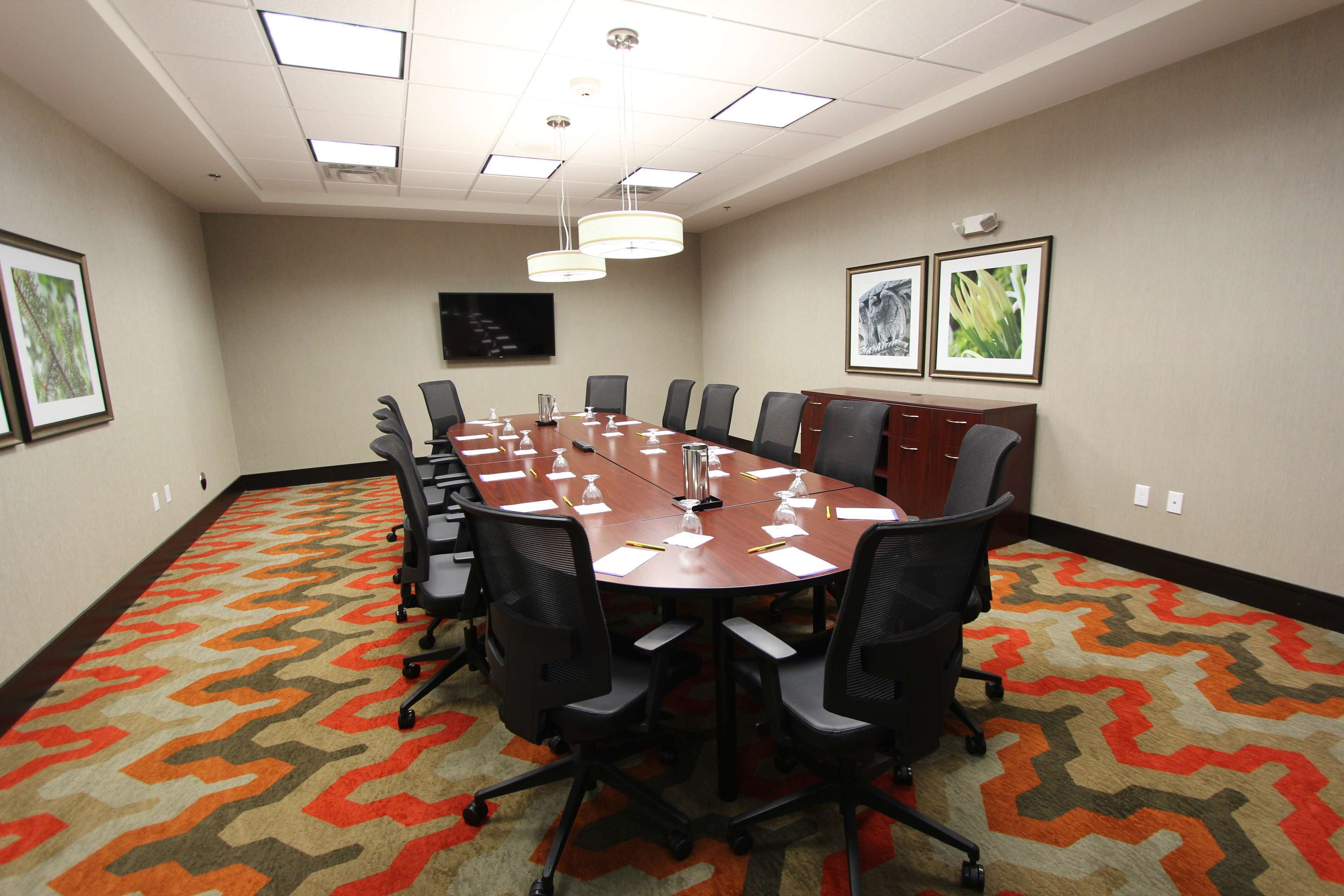 A conference room with a long table, chairs, a projector screen, and framed pictures on the walls.
