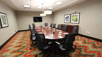 A conference room with a long table, chairs, a projector screen, and framed pictures on the walls.