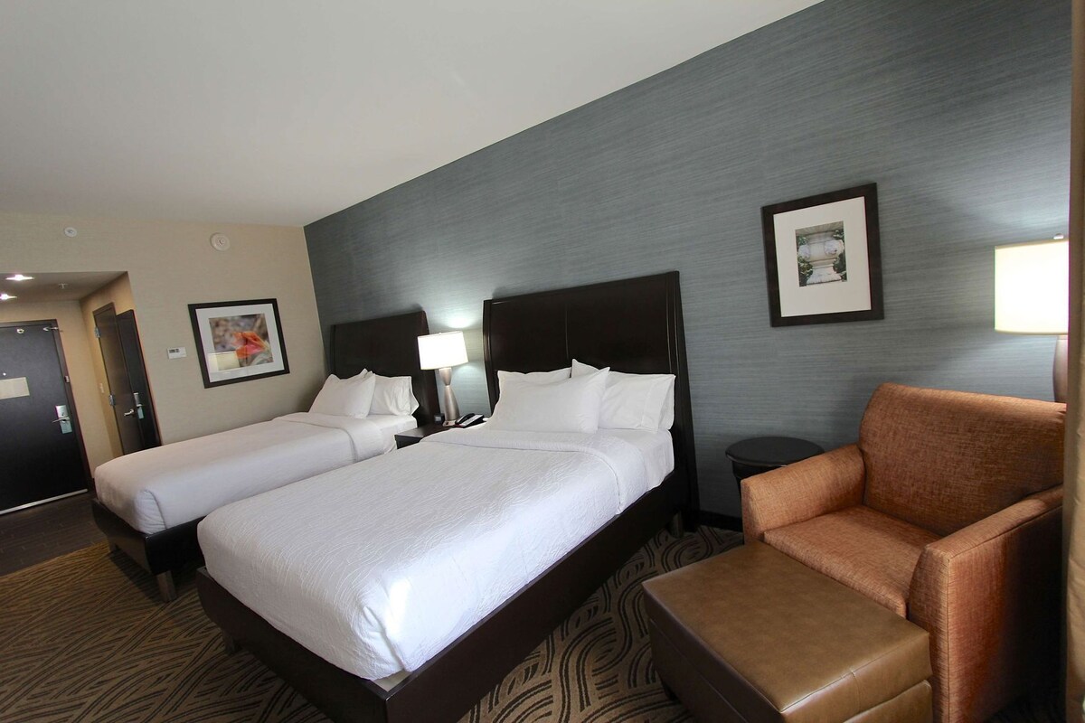 A hotel room with two beds, a sofa, a nightstand with a lamp, and a framed picture on the wall.
