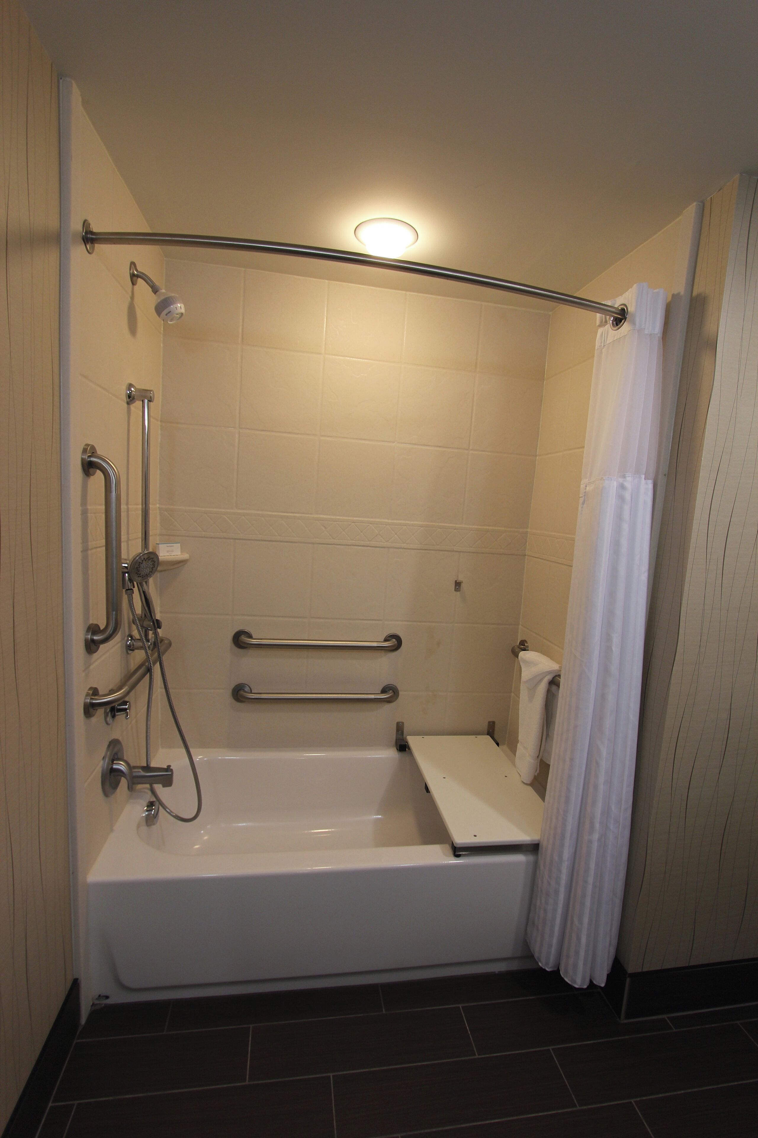 A standard bathroom with a bathtub, grab bars, a showerhead, and a toilet.
