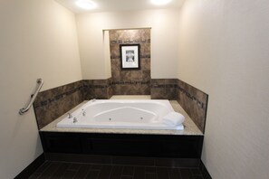 A bathroom with a large bathtub, a framed picture on the wall, and a handrail on the left.