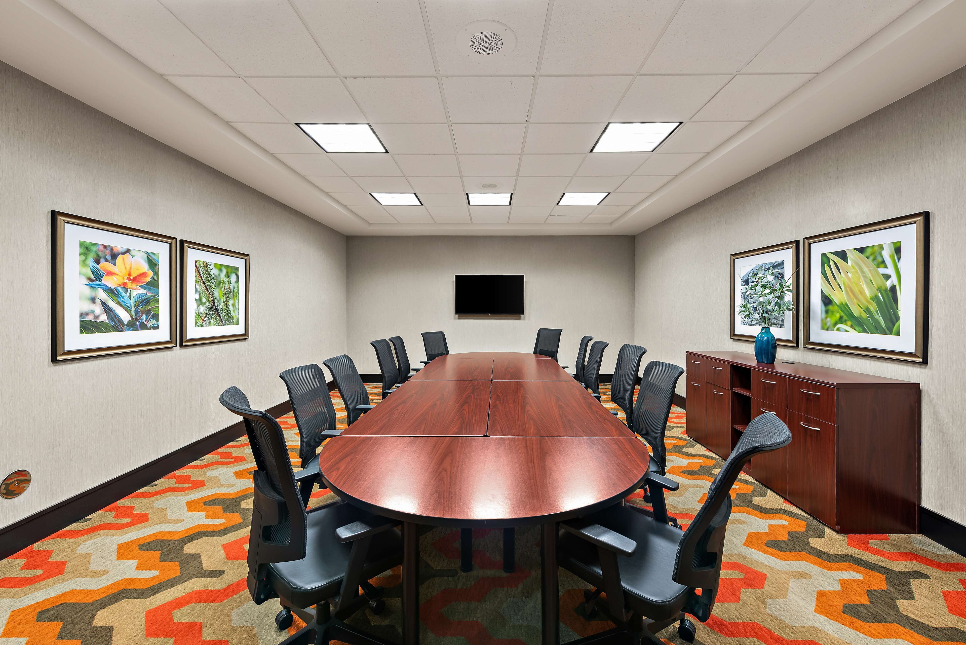 A conference room with a long table, black chairs, a TV on the wall, and framed pictures on the walls.