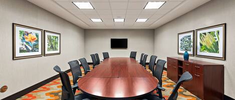 A conference room with a long table, black chairs, a TV on the wall, and framed pictures on the walls.