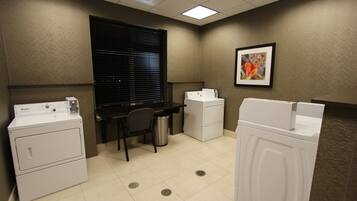 A laundry room with two front-loading washers, a desk, and a trash can.