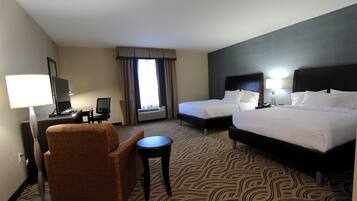 A hotel room with two beds, a desk, a chair, and a lamp.