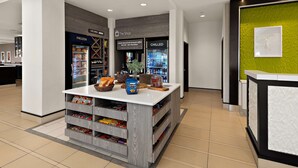 A modern reception area with a counter, a coffee shop named 'The Shop' with a 'FROZEN' and 'CHILLED' beverage section, and a green accent wall. - Hilton Garden Inn Findlay (Findlay)