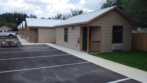 A row of single-story cabins with a covered parking area and picnic tables. - Brush Country Lodge (Pleasanton)