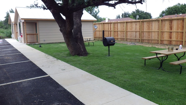 A backyard with a picnic table, a barbecue grill, and a wooden fence. - Brush Country Lodge (Pleasanton)