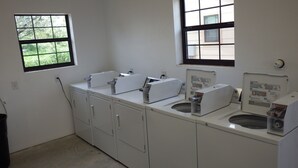 A small, clean laundry room with two sinks, a drying rack, and a window providing natural light. - Brush Country Lodge (Pleasanton)