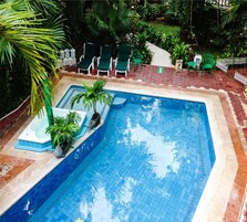 Una piscina con borde de azulejos, rodeada por un camino de ladrillo y sillas verdes.