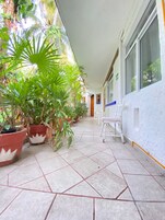 Un pasillo con plantas en macetas, una silla blanca y suelo de baldosas.