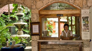 A reception area with a receptionist, a stone wall, a wooden reception desk, a fountain, and a sign indicating the hotel name. - Eco-Hotel El Rey del Caribe (Cancun)