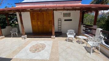 A covered patio with a tiled floor, a wooden door, and white metal chairs.