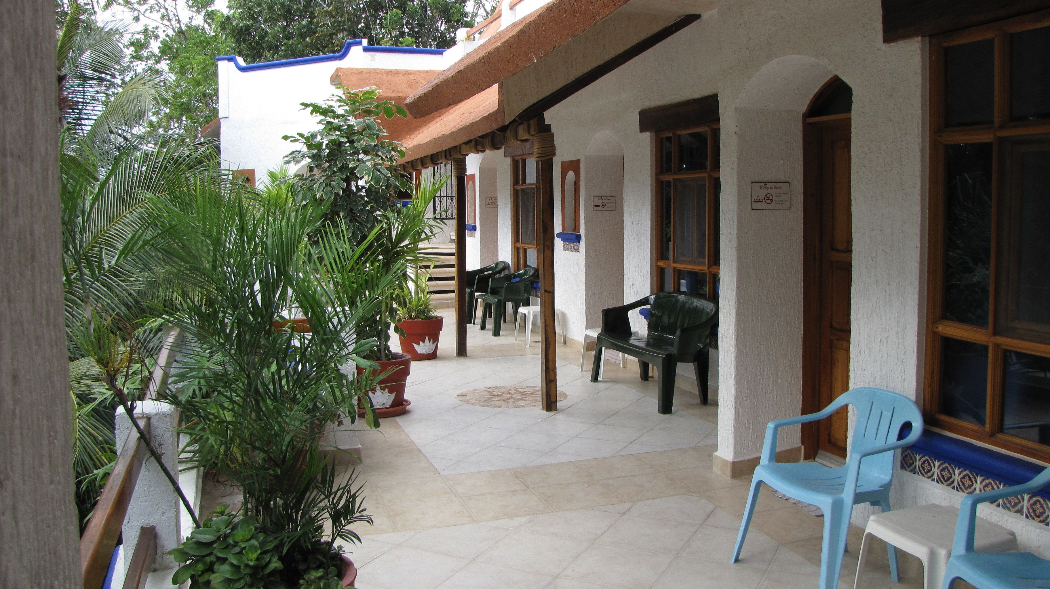 A covered outdoor area with potted plants, a bench, and plastic chairs.