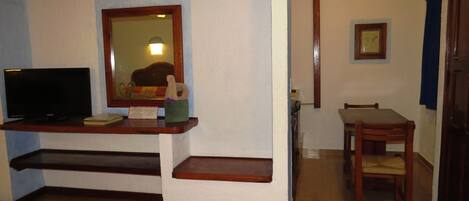 A room with a television on a wooden stand, a mirror above it, and a framed picture on the wall.