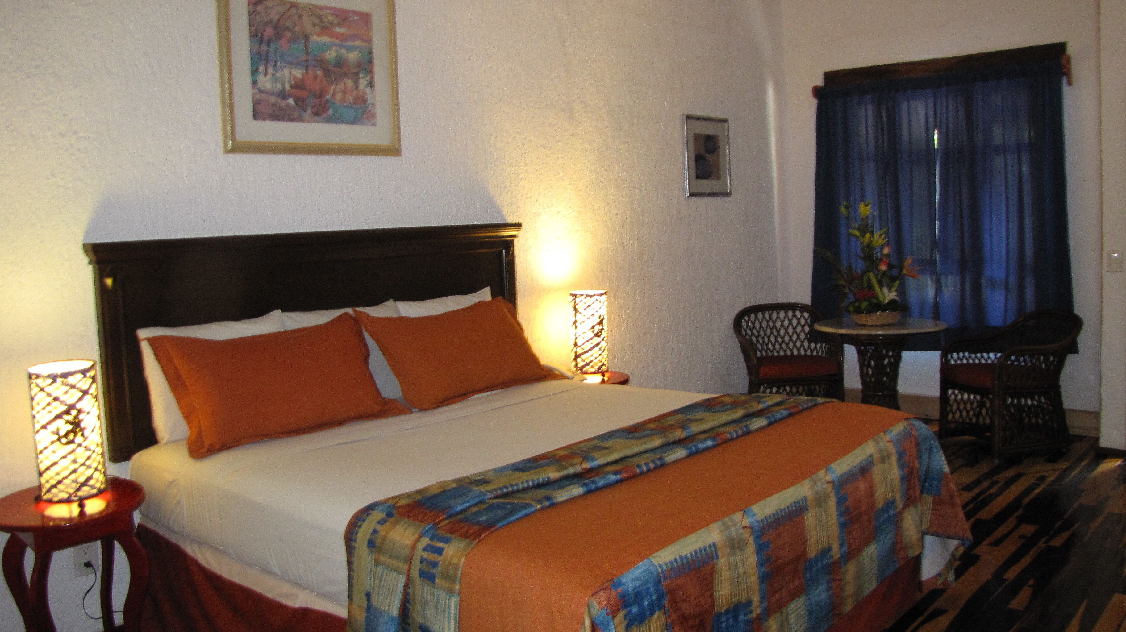 Camera d'albergo con un letto grande, due lampade sui comodini, un tavolino con una sedia e una finestra con tende.