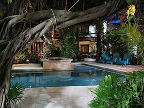 A pool area with a stone fountain, surrounded by lush greenery and blue Adirondack chairs.