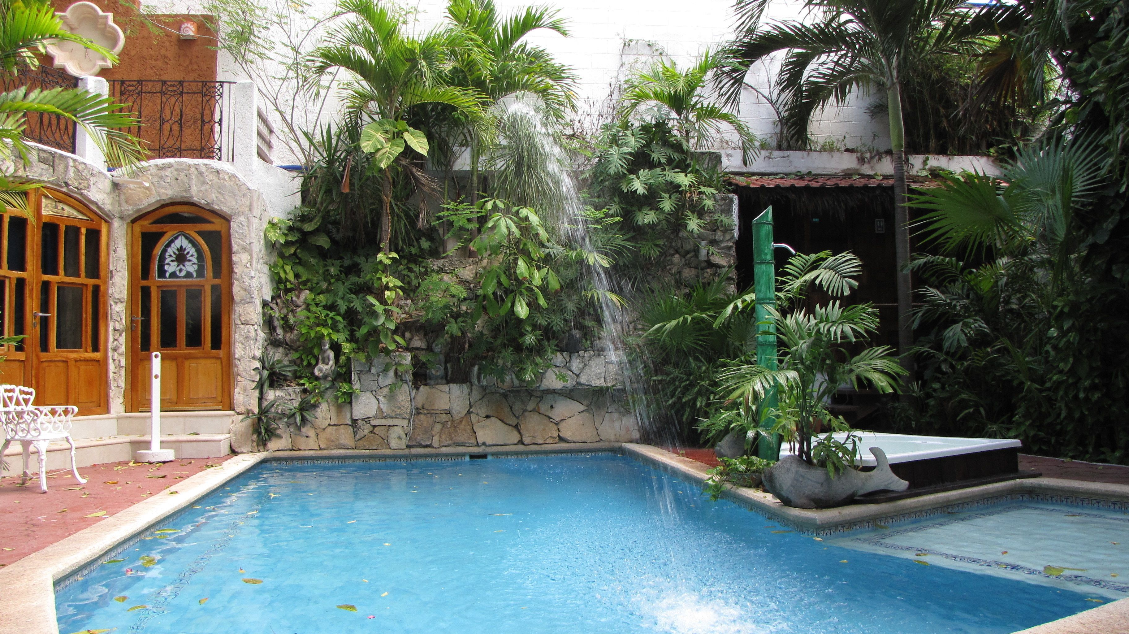 A pool area with a stone wall, a wooden door, and lush greenery.