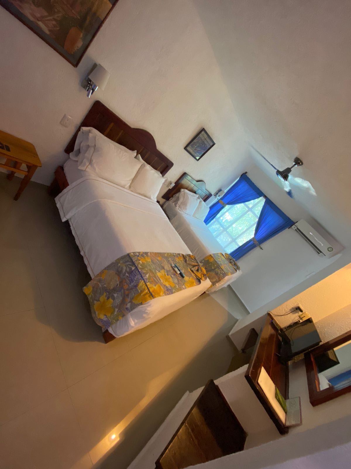 Een hotelkamer met een bed, een bureau, een plafondventilator en een raam met gordijnen.